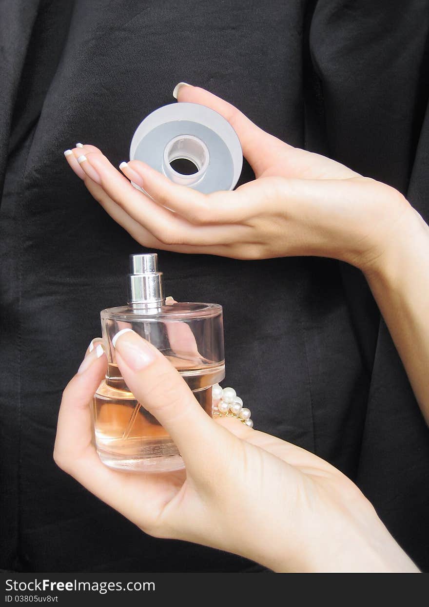 Female hands with perfume bottle on black background