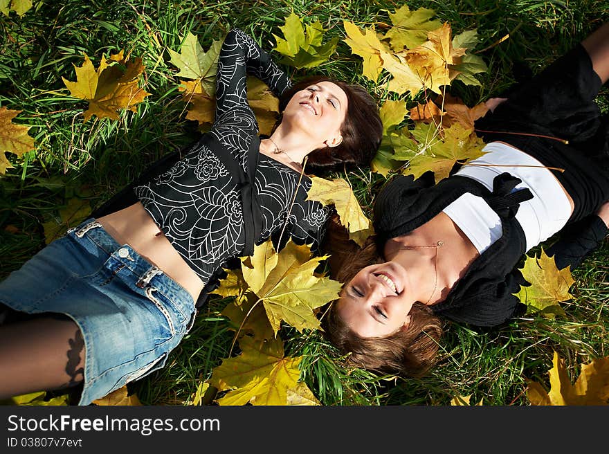 Two happy young woman on green grass and yellow leaves in park. Two happy young woman on green grass and yellow leaves in park