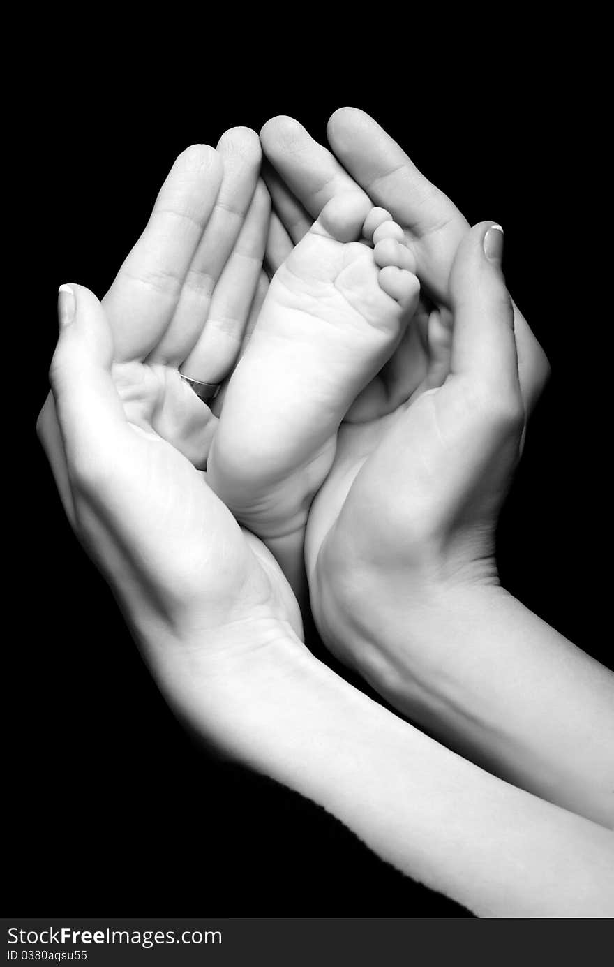 Mother is holding in her hands baby's feet on a black background. Mother is holding in her hands baby's feet on a black background