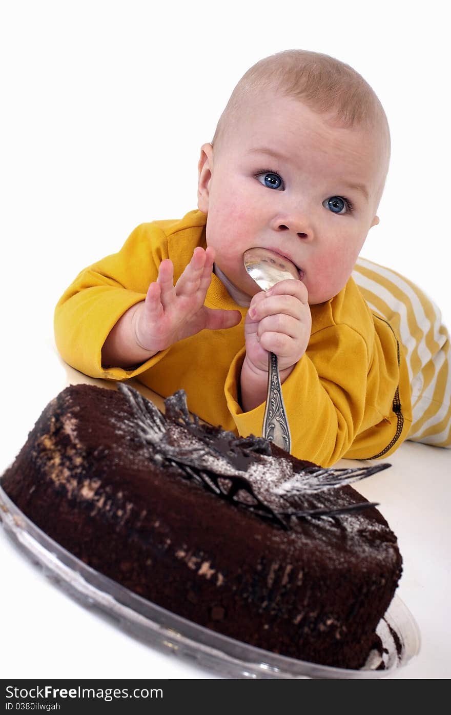 The baby with a big spoon in hand wants to eat chocolate cake