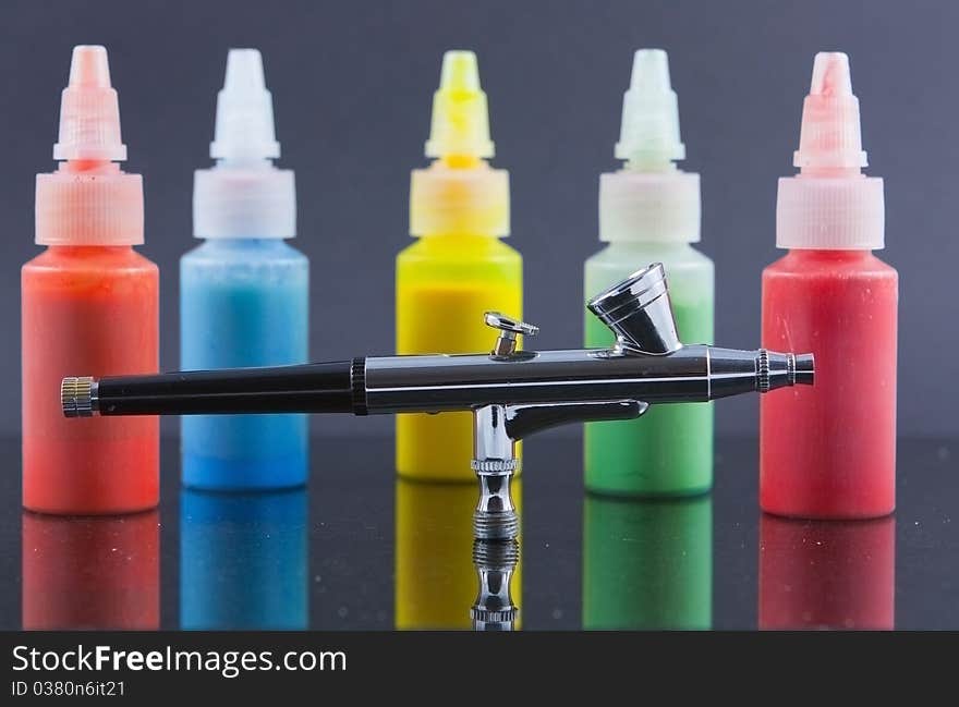 A silver airbrush against a background of out of focus and blurred bottles of spray paint. A silver airbrush against a background of out of focus and blurred bottles of spray paint