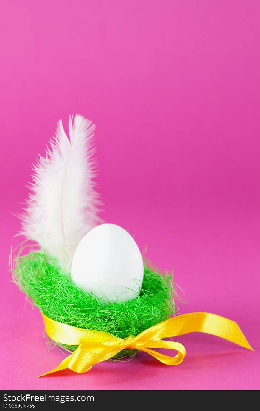 Easter egg in green basket with feather and ribbon in front of pink background with copy space. Easter egg in green basket with feather and ribbon in front of pink background with copy space