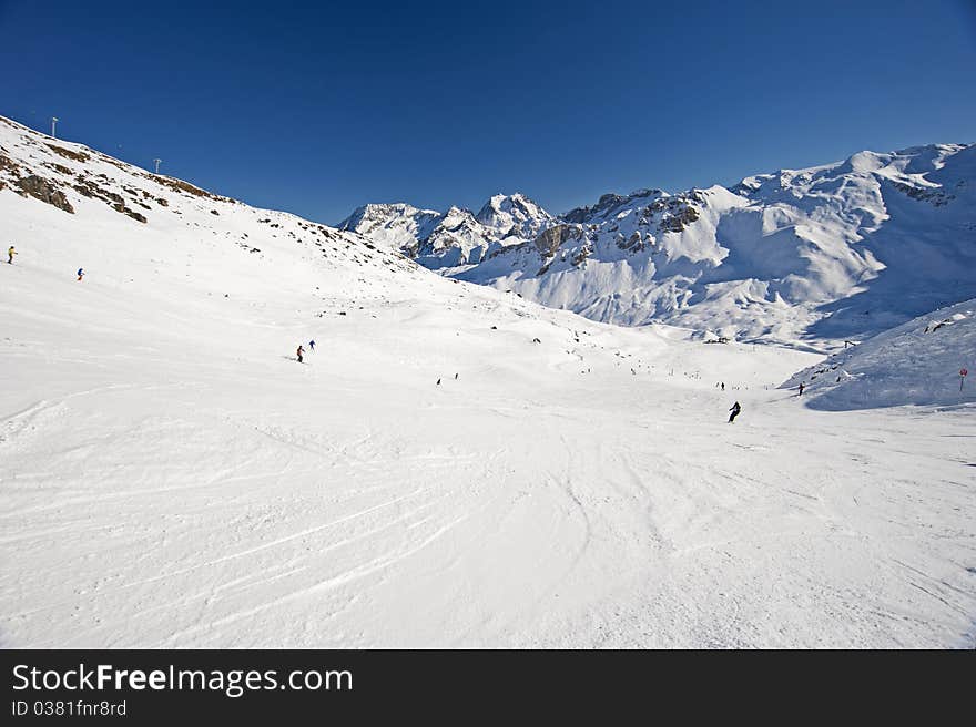 View down a piste with skiers and mountains. View down a piste with skiers and mountains