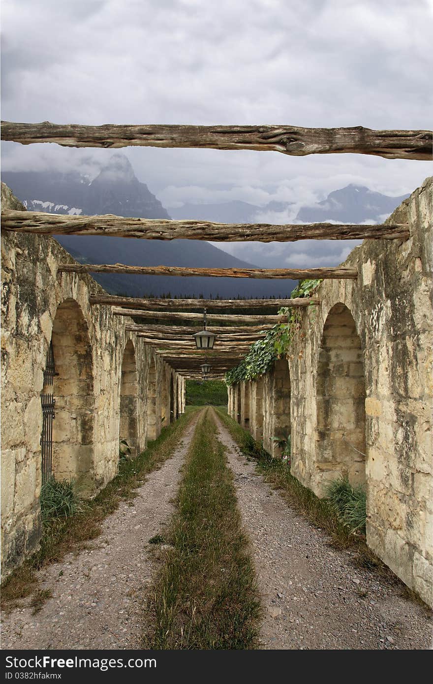 A gravel road flanked by crumbling ruins with mountains in the background.