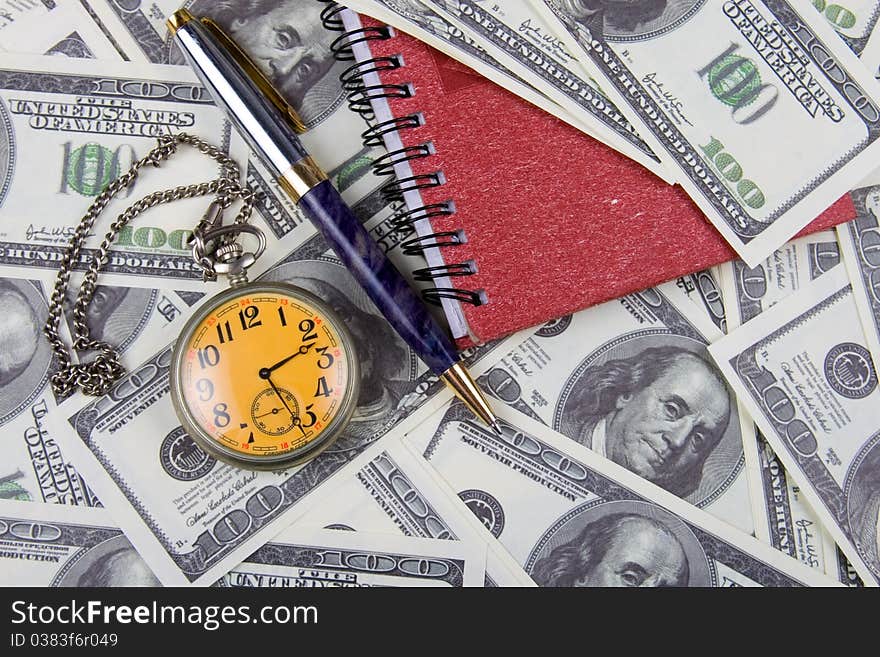 Pocket watch, notebook and pen on a stack of dollars, reflecting time and money