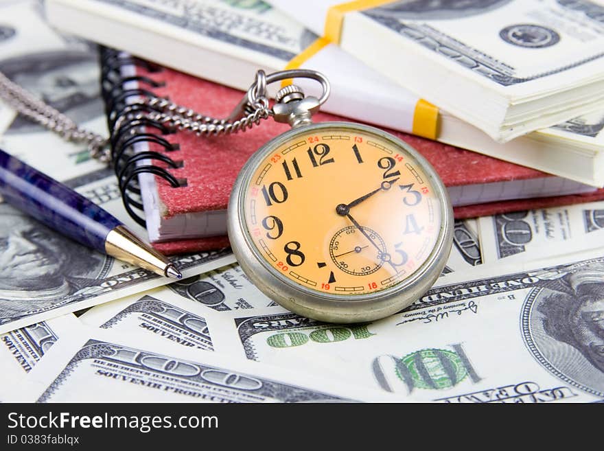 Pocket watch, notebook and pen on a stack of dollars, reflecting time and money