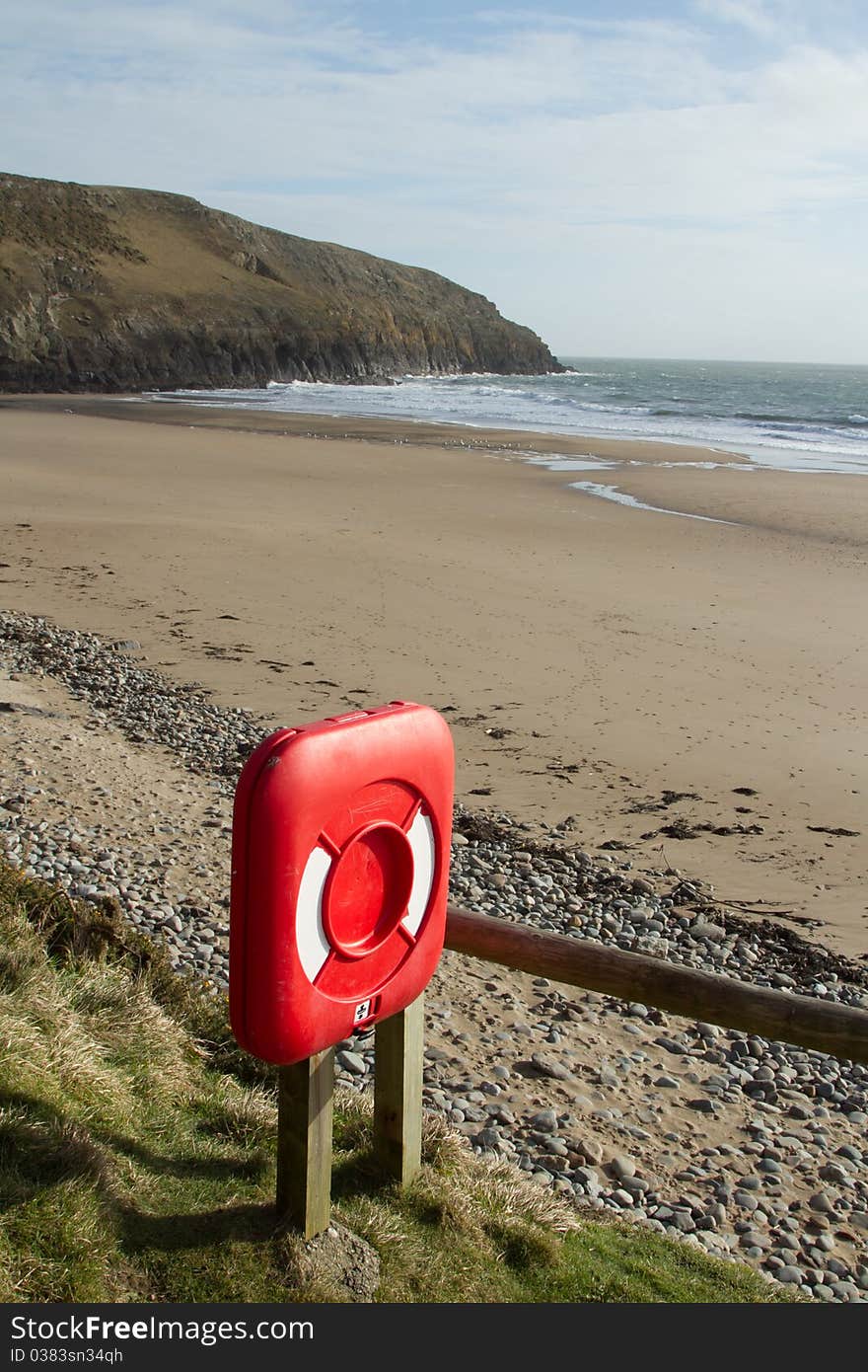 A red container, life saving equipment, placed by a beach with sand, sea and cliff. A red container, life saving equipment, placed by a beach with sand, sea and cliff.