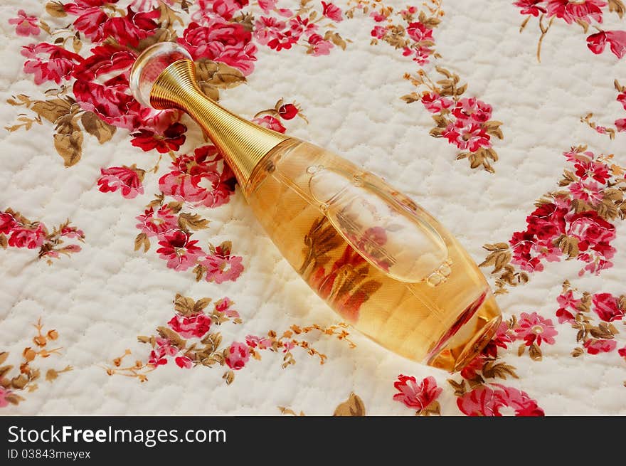 Bottle of perfume on white cloth with pattern of flowers. Bottle of perfume on white cloth with pattern of flowers