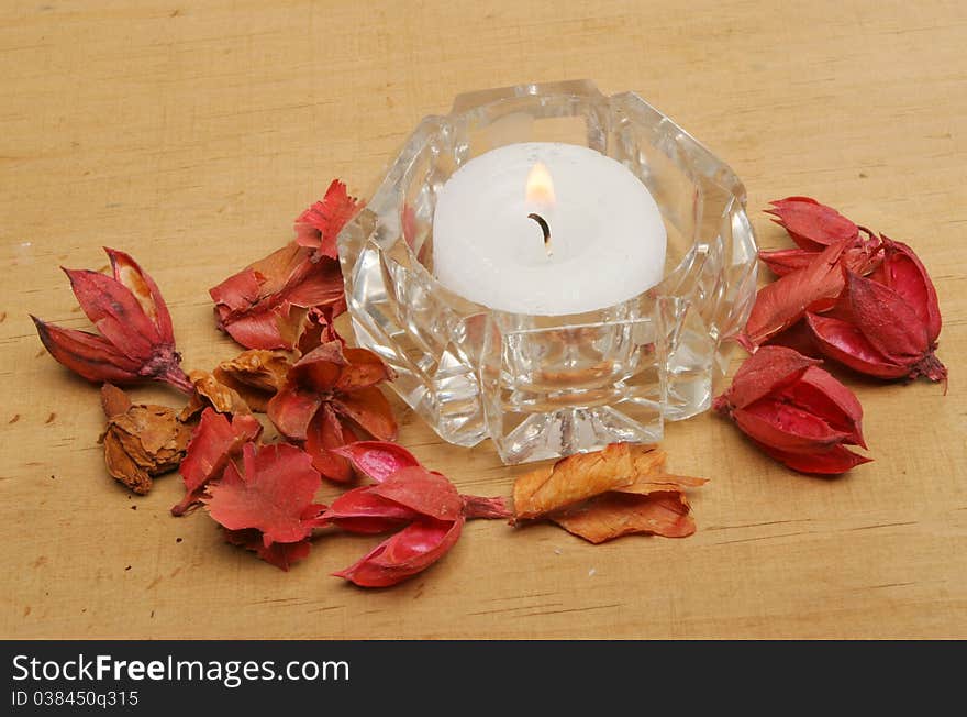 Tea light candle in a crystal glass holder with potpourri on a wooden board