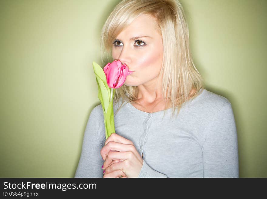 Happy blonde woman holding a single tulip on green background. Happy blonde woman holding a single tulip on green background