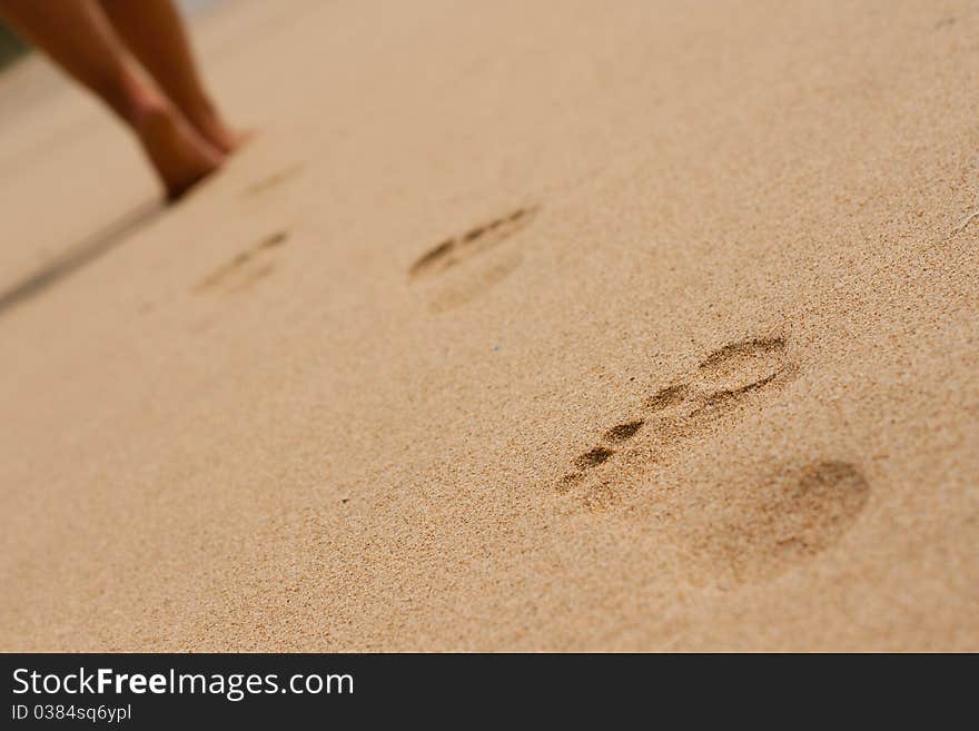 Image of women's legs on the beach and footprints in the sand