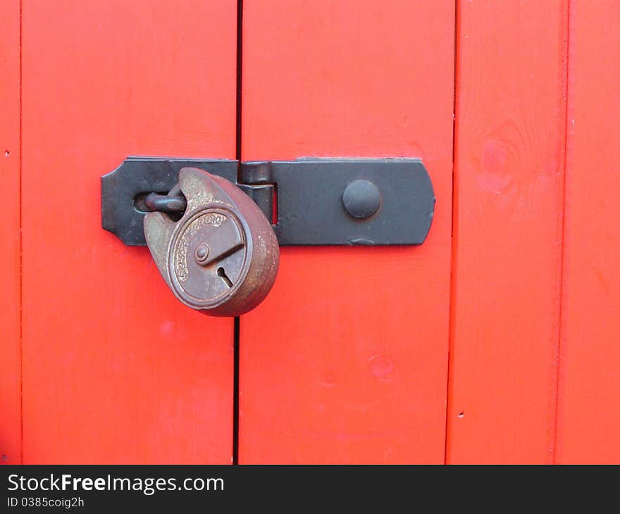 Red painted wooden door closed with a hasp and padlock. Red painted wooden door closed with a hasp and padlock