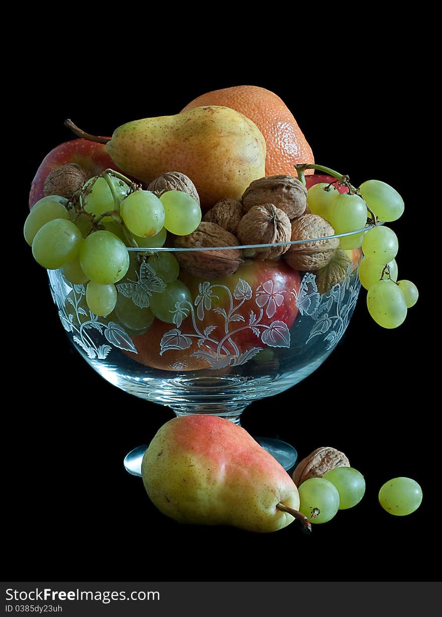 Pears, oranges grapes walnuts displayed in crystal bowl and isolated on black background. Pears, oranges grapes walnuts displayed in crystal bowl and isolated on black background