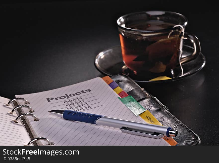 Pen a notebook and a tea cup against a dark background. Pen a notebook and a tea cup against a dark background