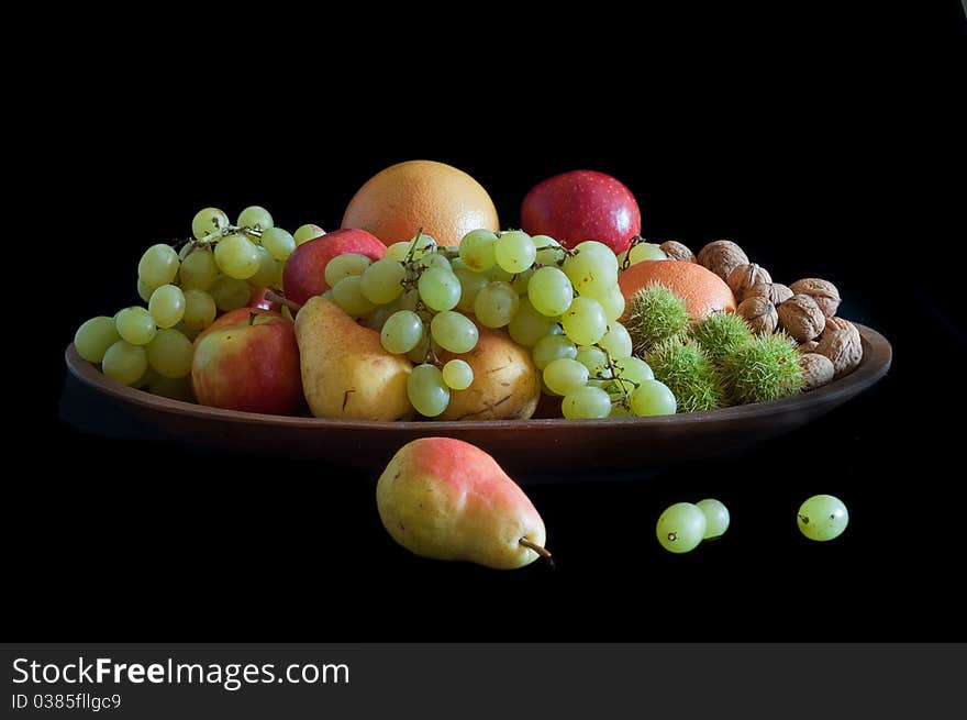 Pears, oranges grapes walnuts, chestnuts in outer covering, displayed in teak wood tray and isolated on black background. Pears, oranges grapes walnuts, chestnuts in outer covering, displayed in teak wood tray and isolated on black background