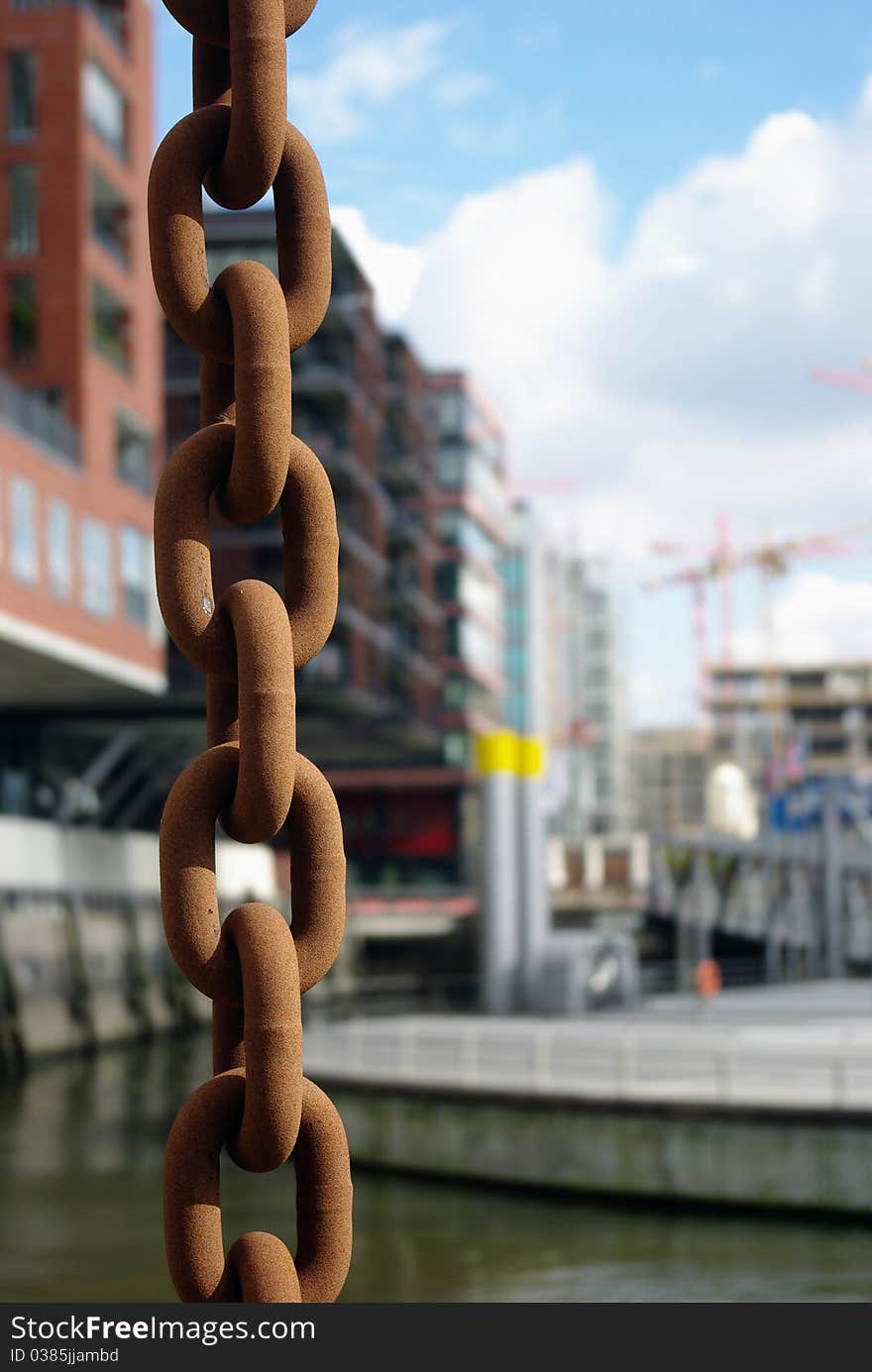 Harbour scene with rusty chain in the foreground, modern architecture and a pier in the background