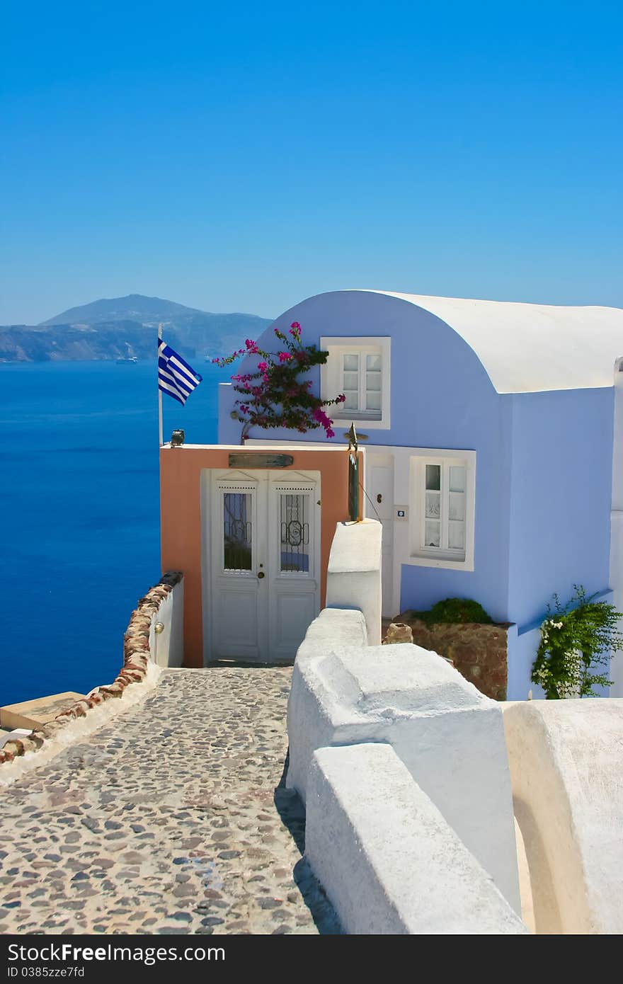 Beautiful house with greece national flag on the street in Santorini, Oia. Aegean sea in a background, Greece. Beautiful house with greece national flag on the street in Santorini, Oia. Aegean sea in a background, Greece.