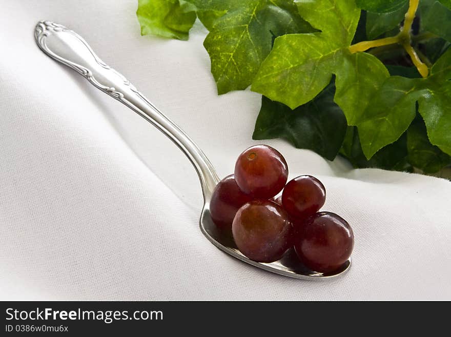 Red grapes piled on spoon on white cloth with leaves on background. Red grapes piled on spoon on white cloth with leaves on background