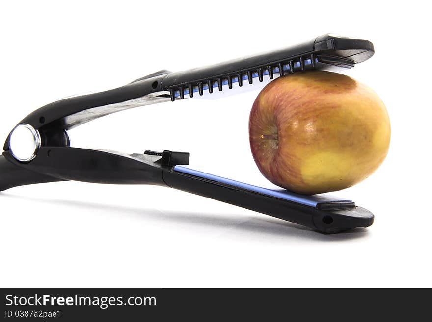 The open jaws of a flat curling iron about to bite an apple on a white background. The open jaws of a flat curling iron about to bite an apple on a white background