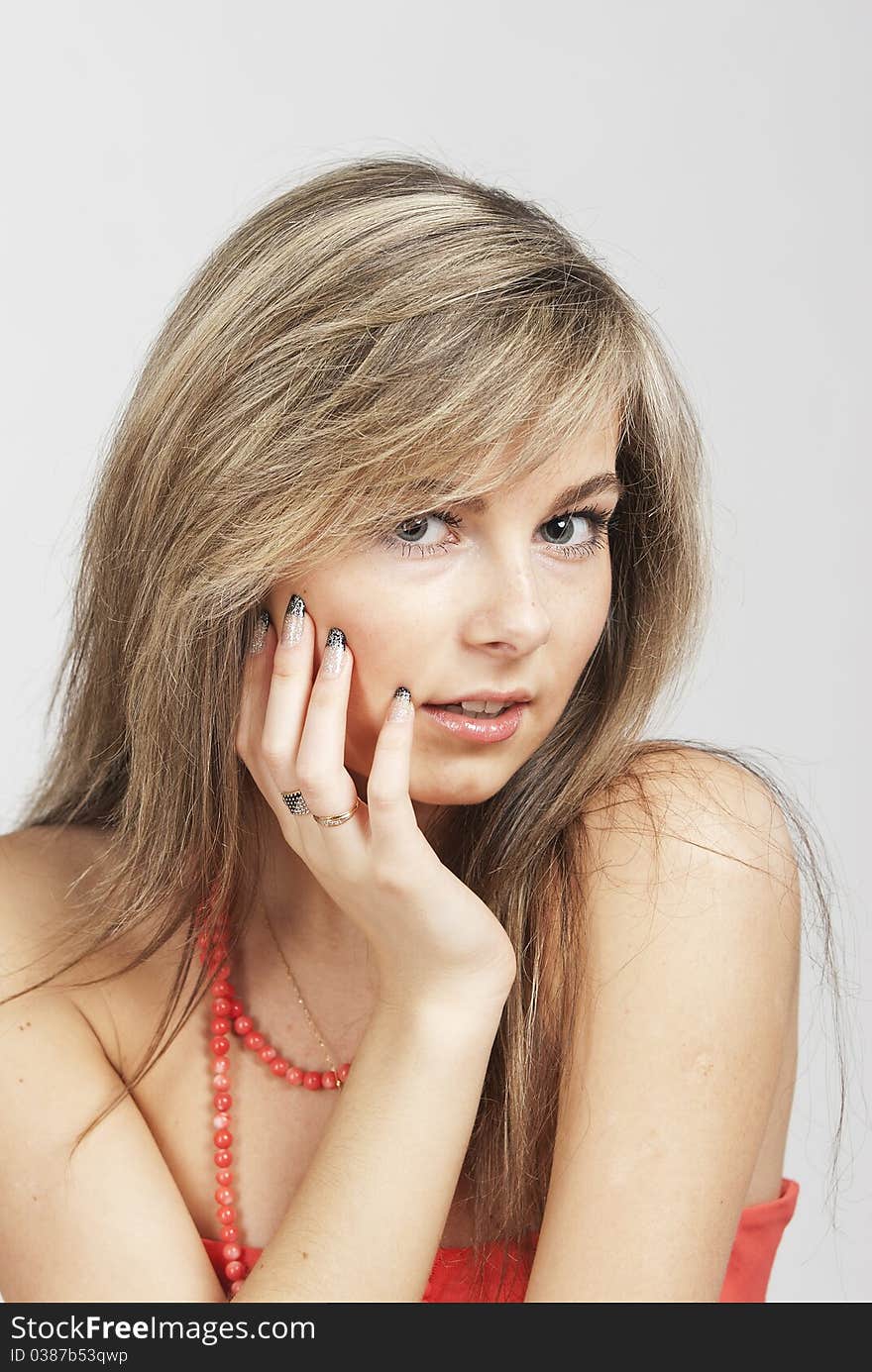 The young beautiful girl the blond with a long straight hair in a red dress and a coral beads smiles in the chamber. The young beautiful girl the blond with a long straight hair in a red dress and a coral beads smiles in the chamber