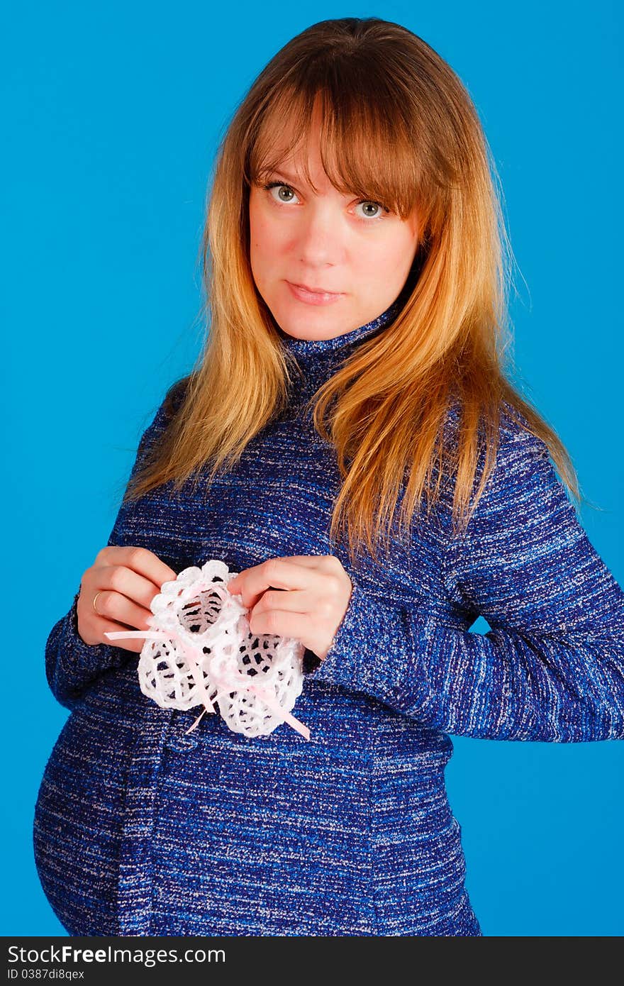 Beautiful pregnant woman with baby's bootees on blue background