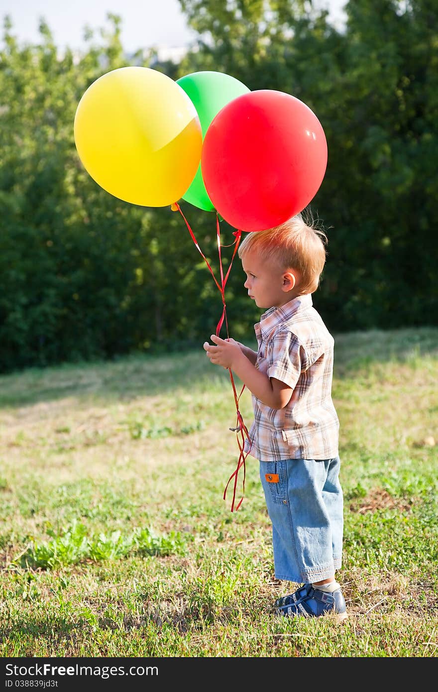 A cute boy is standing on a lawn with colorful balloons