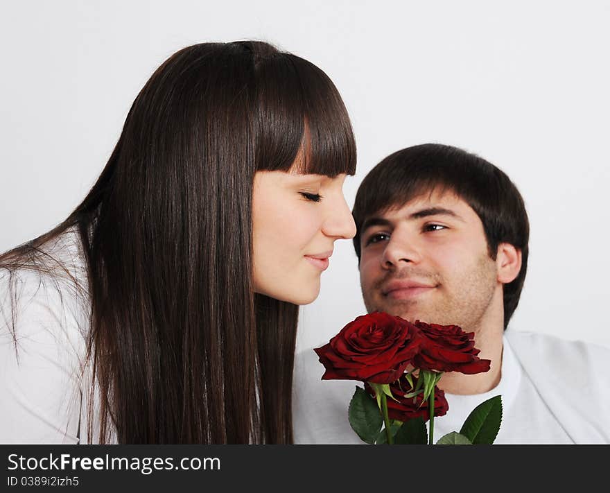 Young pretty woman smelling roses, her boyfriend behind
