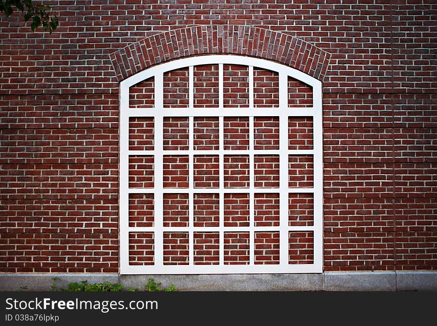 A white window frame topped by an arch, over a red brick wall, seems to be a window to nowhere.