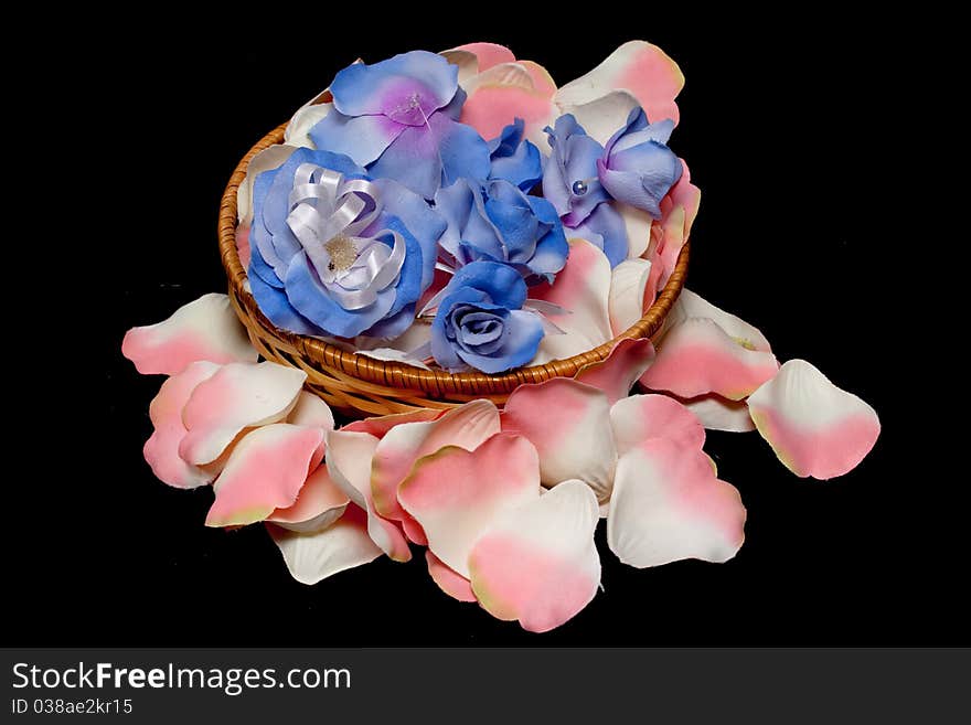 A basket with artificial flowers on white and pink rose textile petals on black. A basket with artificial flowers on white and pink rose textile petals on black