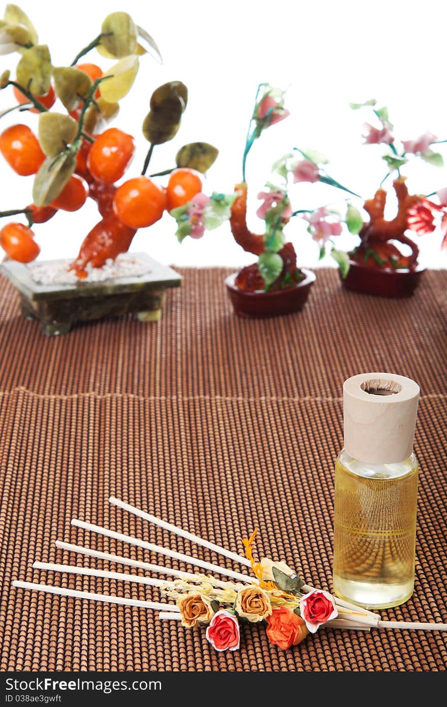 Glass bottle with yellow oil and small flowers lay on brown mat. Stone trees at the background. Glass bottle with yellow oil and small flowers lay on brown mat. Stone trees at the background