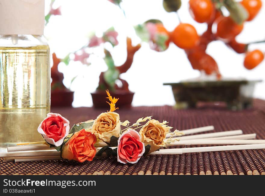 Glass bottle with yellow oil and small flowers lay on brown mat. Stone trees at the background. Glass bottle with yellow oil and small flowers lay on brown mat. Stone trees at the background