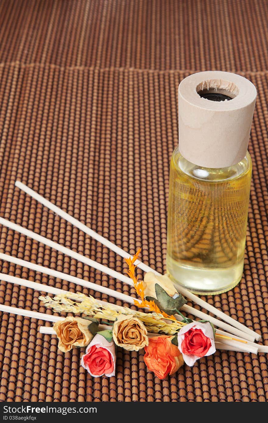 Glass bottle with yellow oil and small flowers lay on brown mat. Glass bottle with yellow oil and small flowers lay on brown mat