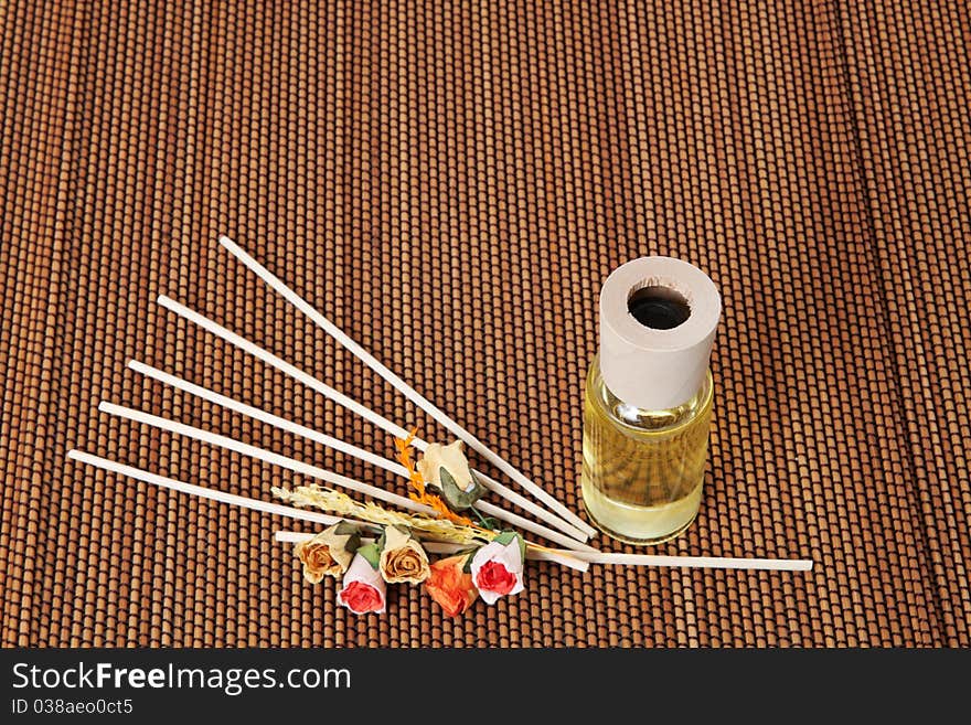 Glass bottle with yellow oil and small flowers lay on brown mat. Glass bottle with yellow oil and small flowers lay on brown mat