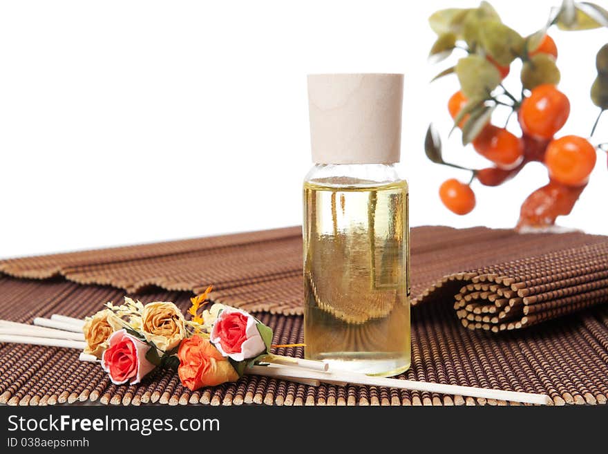 Glass bottle with yellow oil and small flowers lay on brown mat. Stone trees at the background. Glass bottle with yellow oil and small flowers lay on brown mat. Stone trees at the background