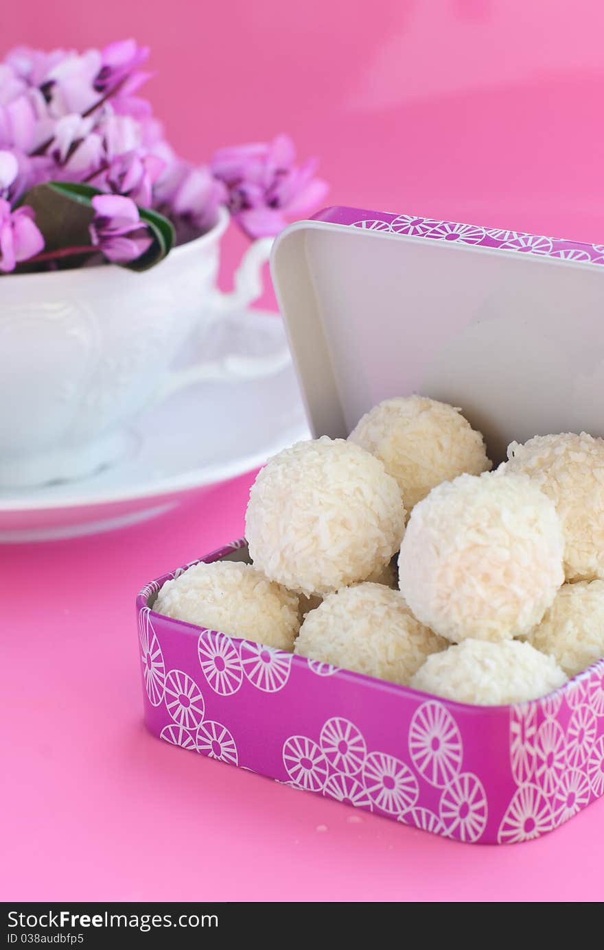 White candies into a pink box, white cup with purple spring flowers on pink background. White candies into a pink box, white cup with purple spring flowers on pink background