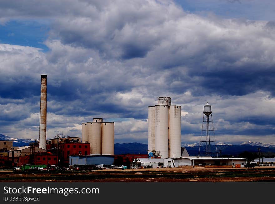 Old factory with blue sky lots of white clouds near boulder Colorado, silos, smoke stacks, water tower and mountains