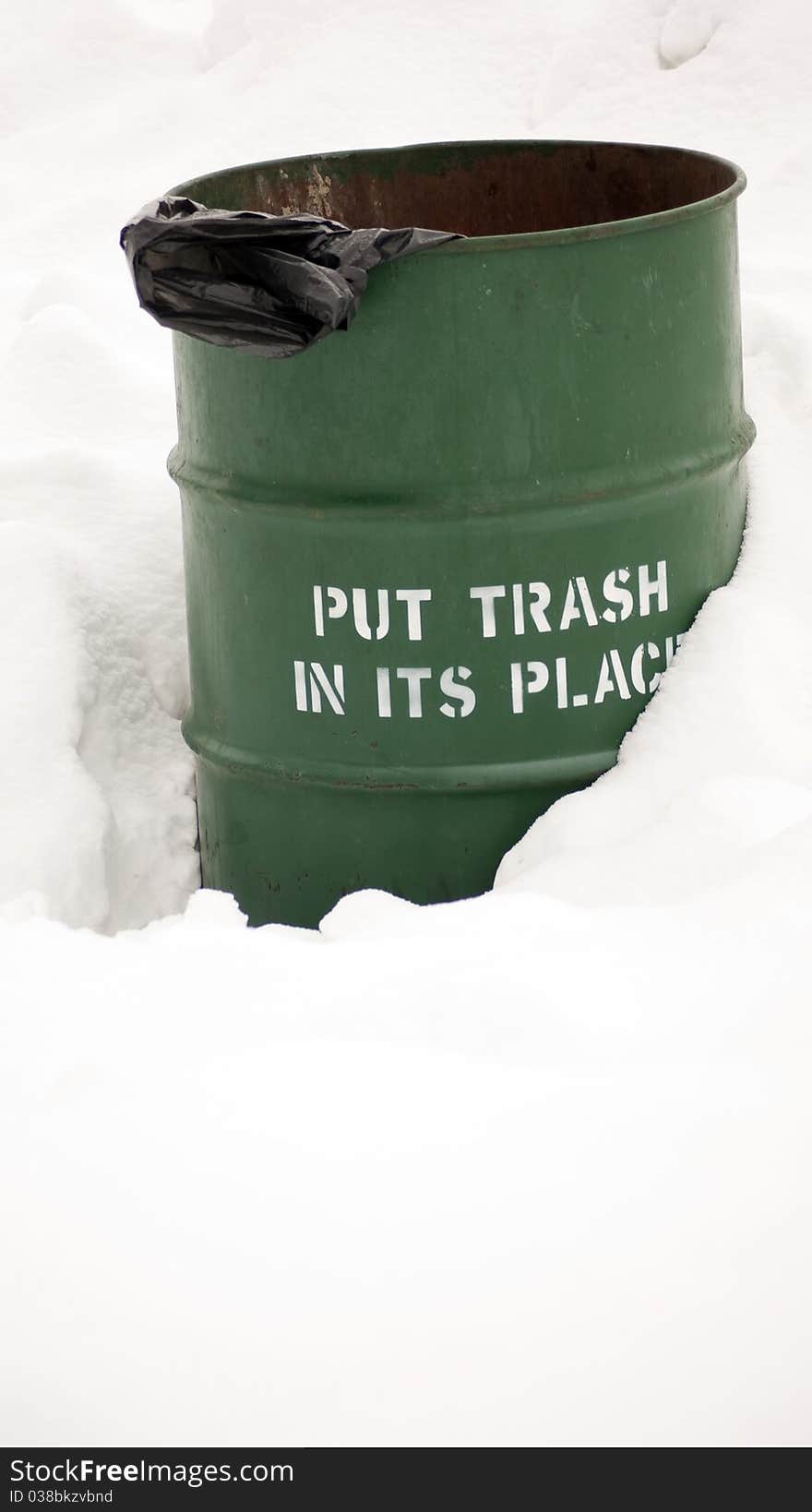 Green trash barrel partly buried in the snow bearing the stenciled sign: Put trash in its place. Green trash barrel partly buried in the snow bearing the stenciled sign: Put trash in its place.