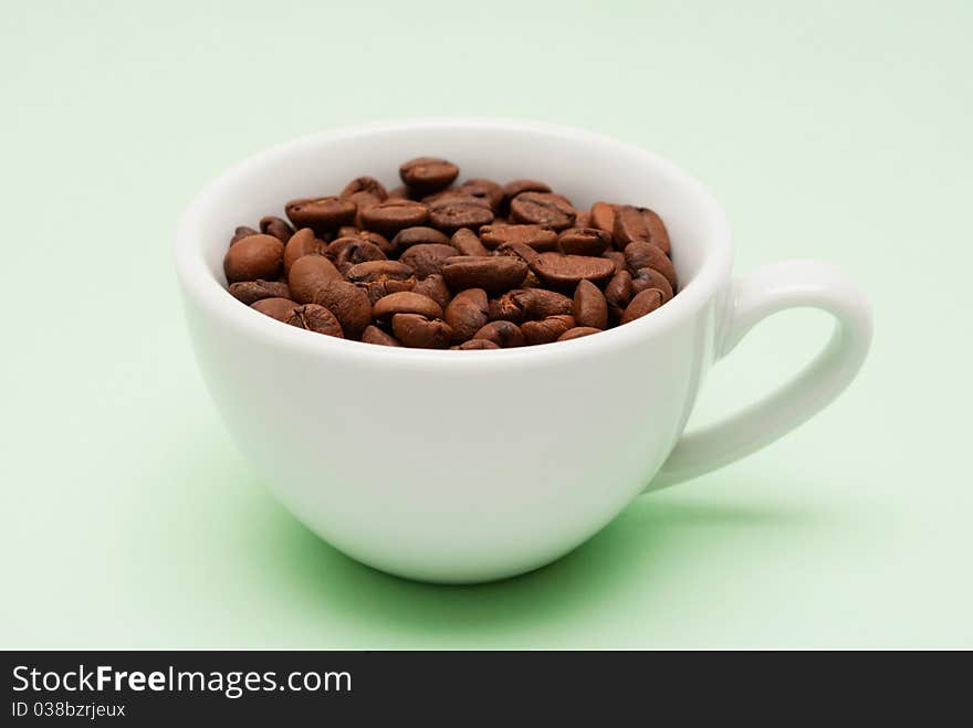 Brown roasted coffee beans in a white cup