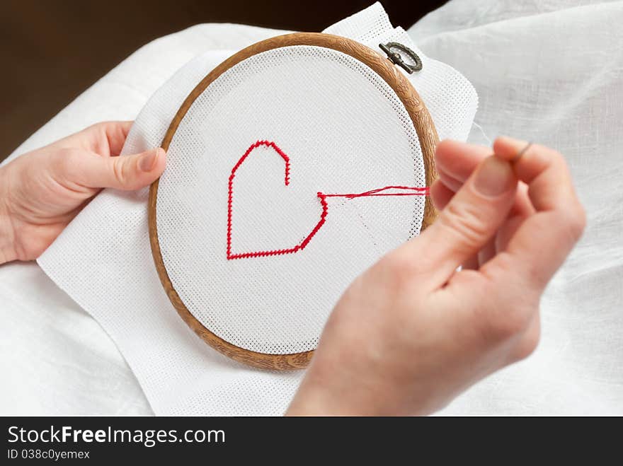 A female hands embroidering red heart. A female hands embroidering red heart