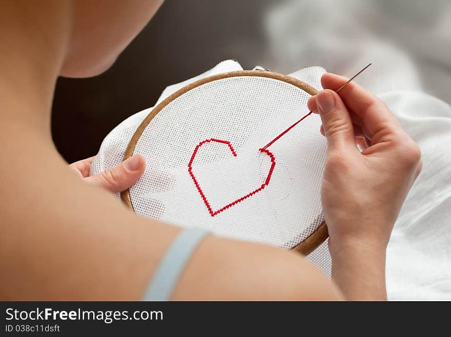 Young woman embroidering a red heart. Young woman embroidering a red heart