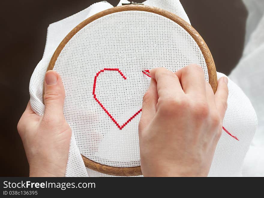 Female hands with tambour and needle, embroidering valentine heart