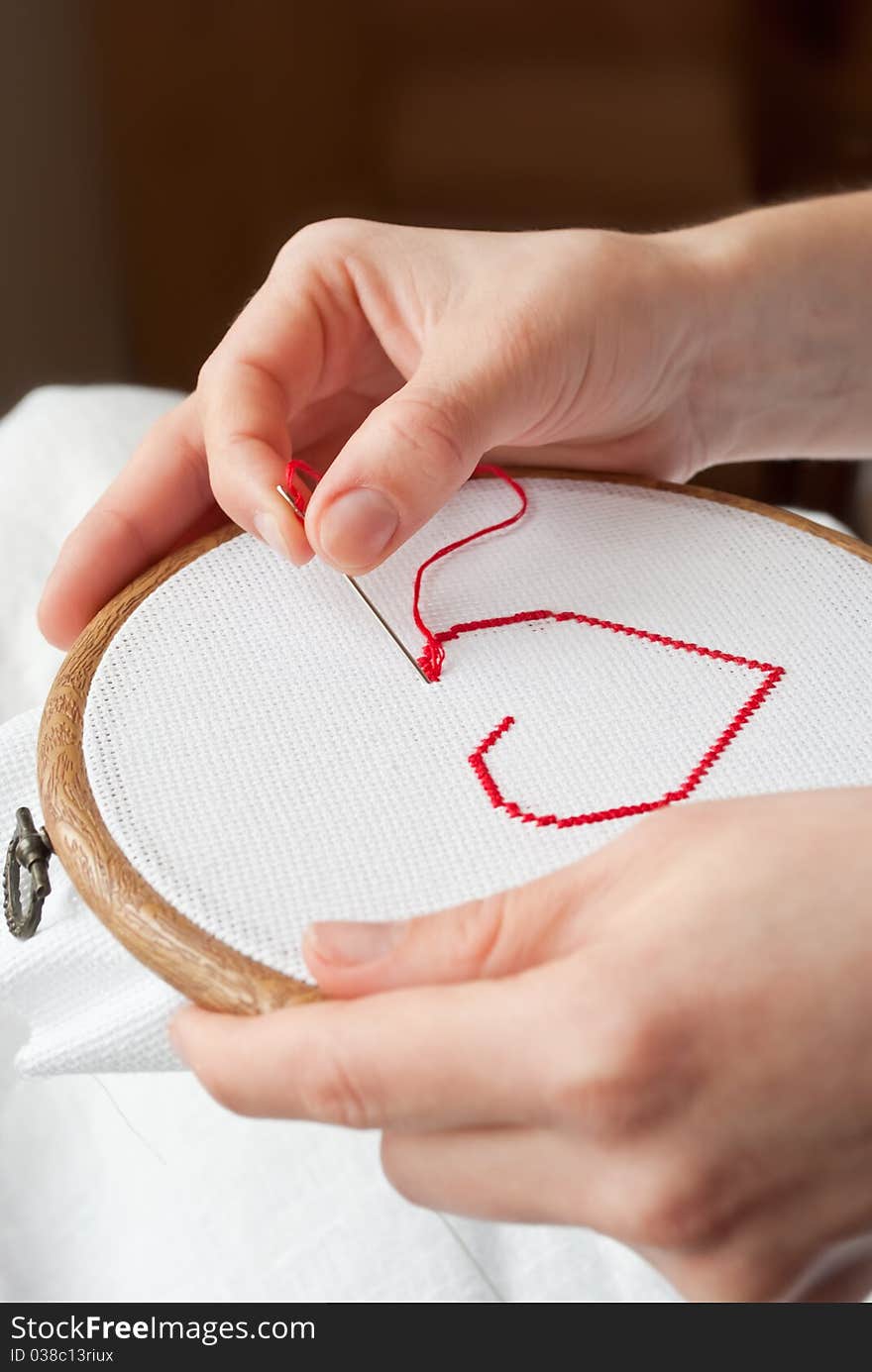 A female hands embroidering red heart. A female hands embroidering red heart