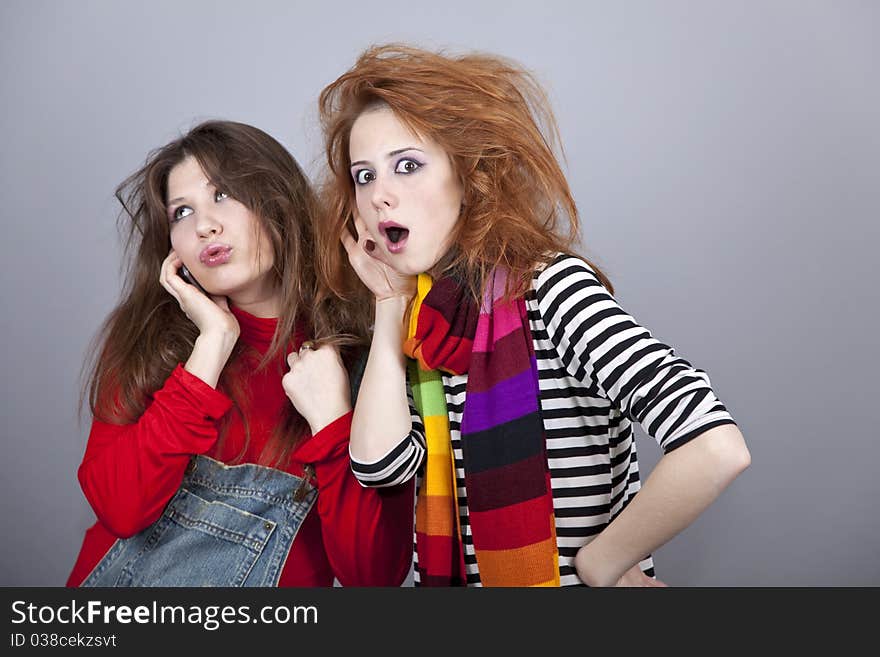 Two funny girls. One of them calling by phone. Studio shot.