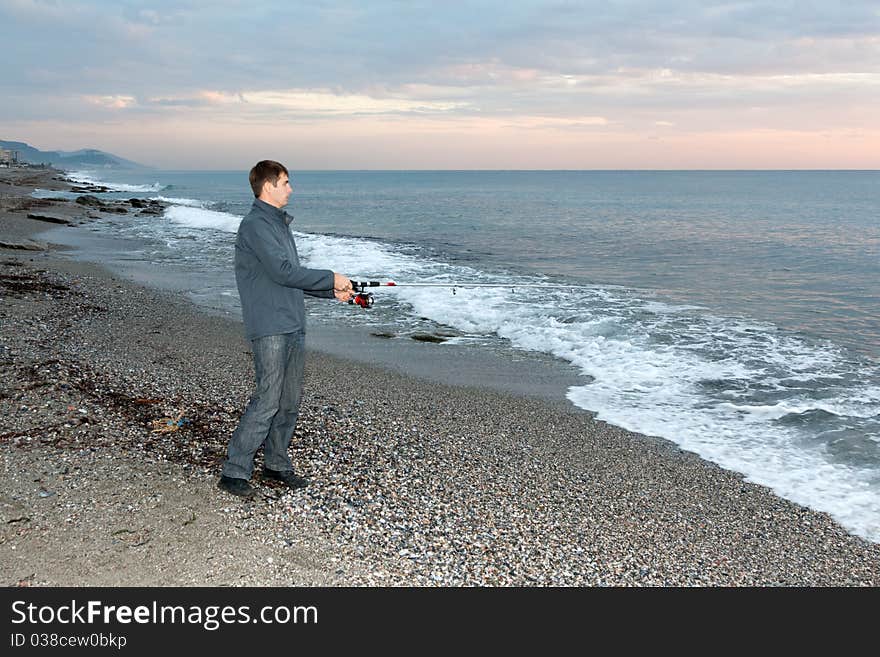 Fisherman on the shore of evening sea