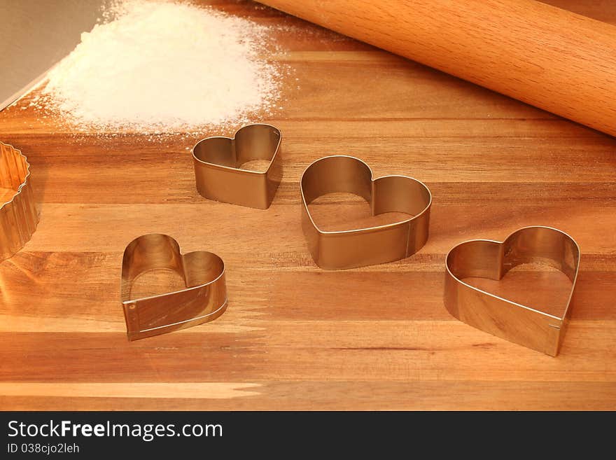 Heart shaped cookie cutters, rolling pin & sifted flour on cutting board