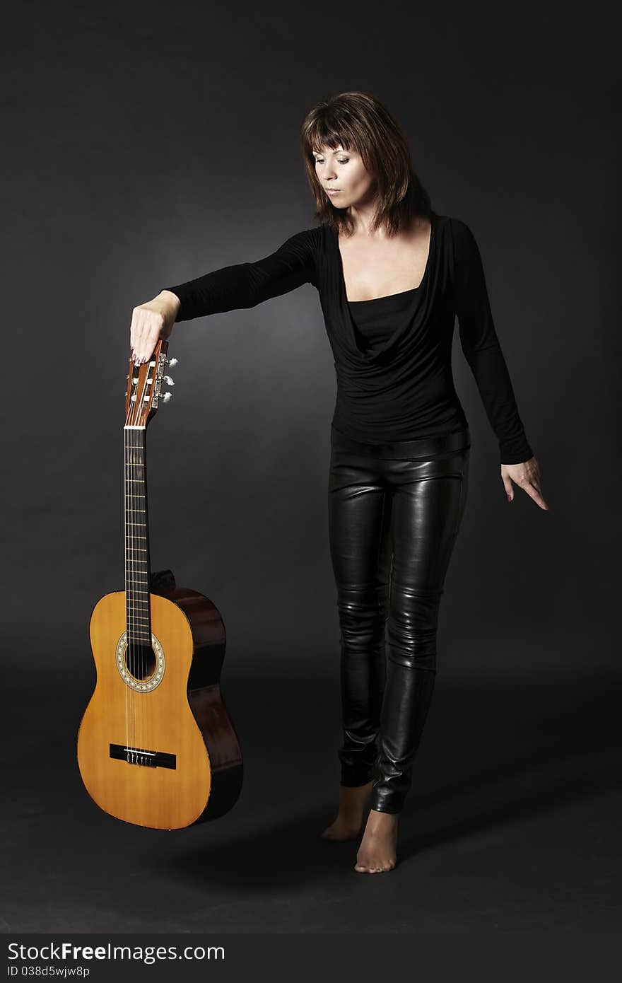 Young woman in black holding guitar in one hand pretending to drop it, isolated on black background. Young woman in black holding guitar in one hand pretending to drop it, isolated on black background.