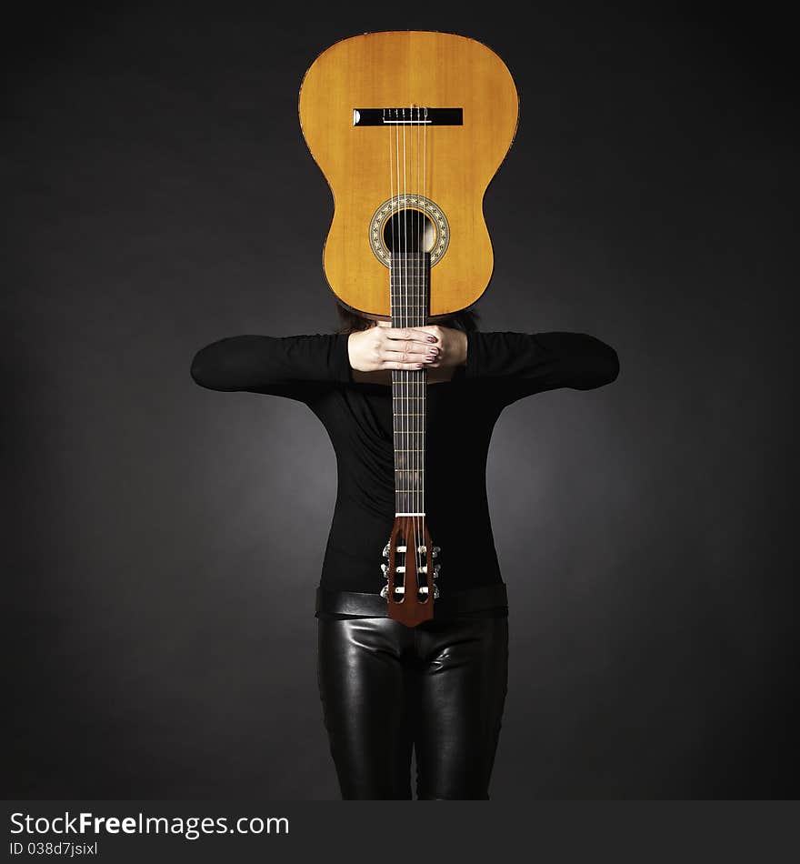 Woman in black holding guitar in front of face, creating a cross shape, isolated on black background. Woman in black holding guitar in front of face, creating a cross shape, isolated on black background.