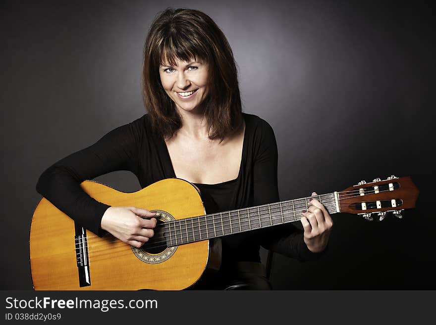 Smiling girl in black sitting and playing on guitar looking straight, isolated on black background. Smiling girl in black sitting and playing on guitar looking straight, isolated on black background.