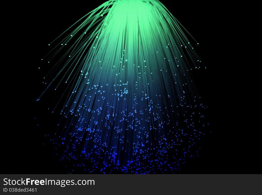 Blue and green coloured fibre optic light strands cascading down with a black background. Blue and green coloured fibre optic light strands cascading down with a black background.