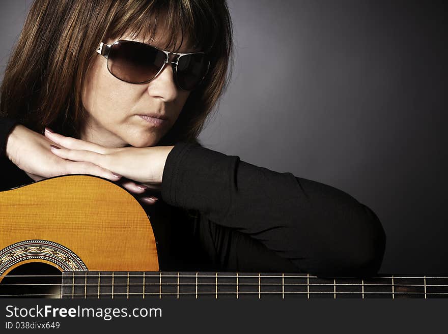 Close up of cool young woman in black leaning on guitar looking down, isolated on black. Close up of cool young woman in black leaning on guitar looking down, isolated on black.